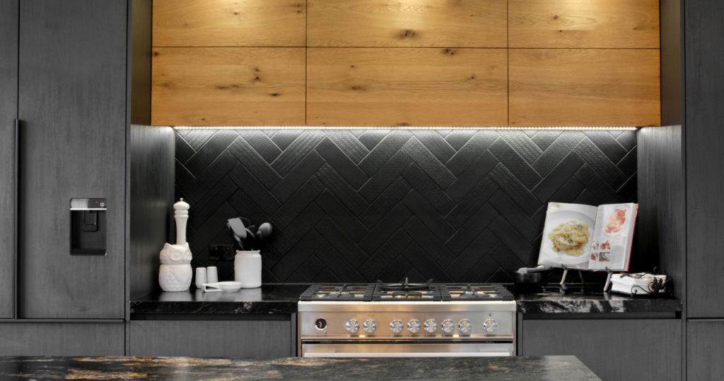 Close-up of kitchen showcasing dark cabinetry, dark tiled splashback, and wooden upper cabinetry.