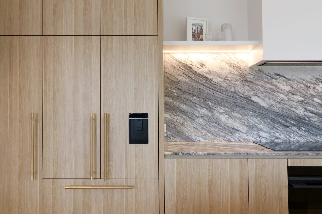 Integrated fridge with thick Melteca Classic Oak panels, brass handle, Sensa Sant Angelo granite benchtop, and open shelving.