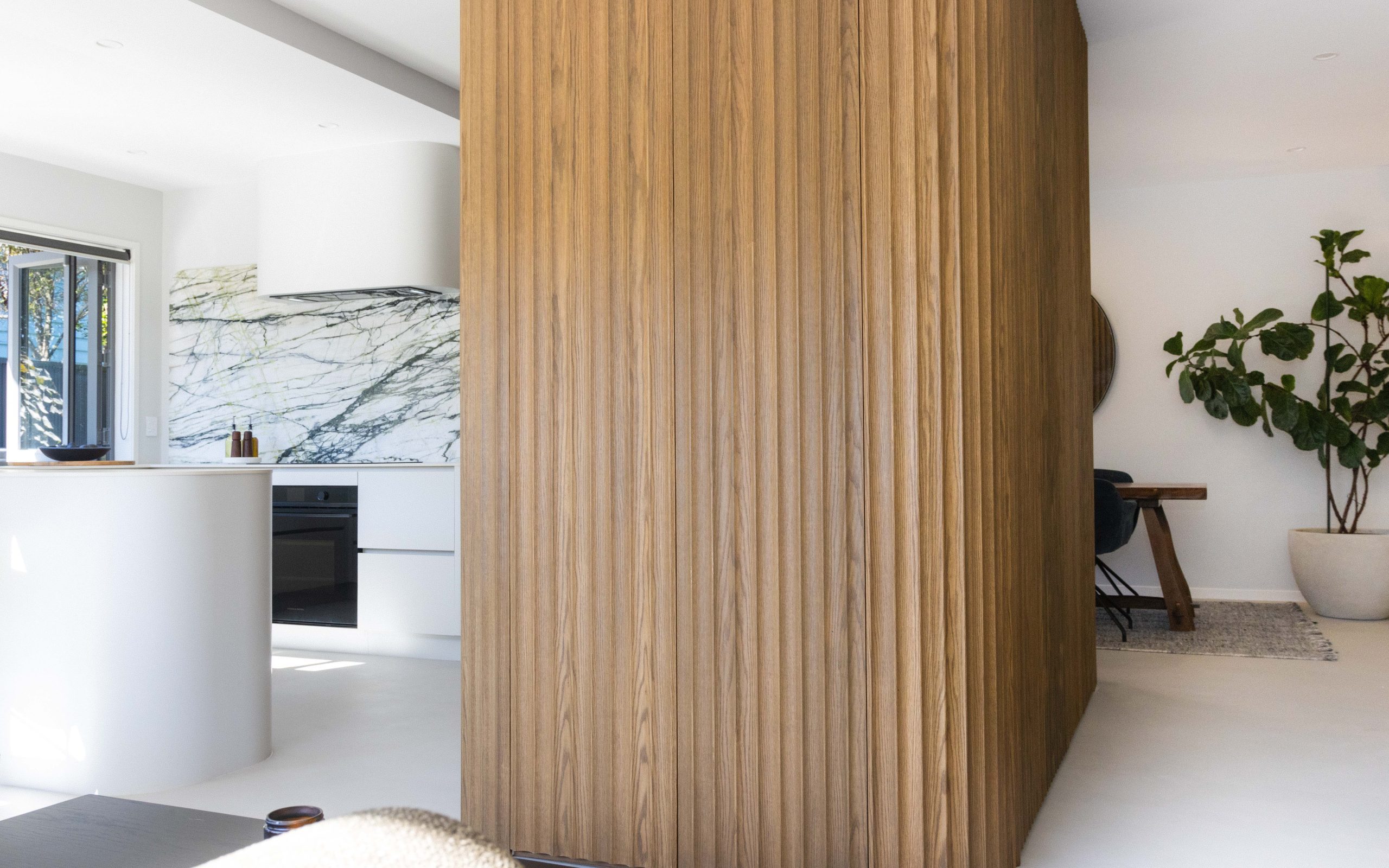 Central tall kitchen units in Ripple Flex oak flanked by custom Melteca Aged Walnut and Baikal Natural cabinetry in a modern Bayswater kitchen by Fluid Interiors.