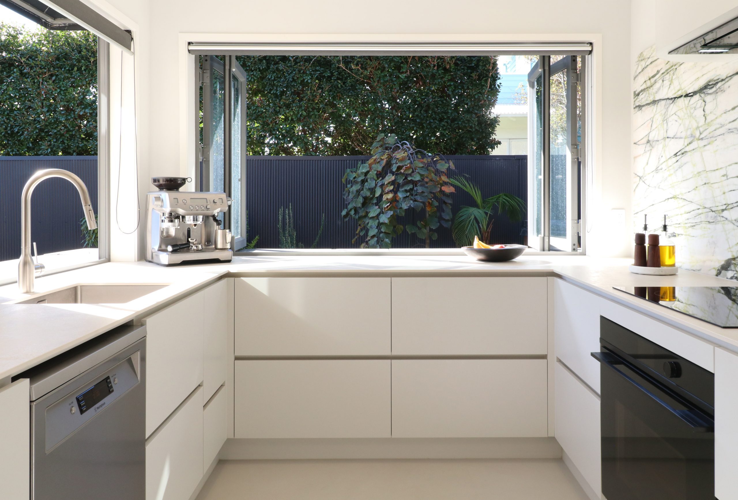 Melteca Baikal Natural base cabinetry with negative detail handles, positioned under a window in the Bayswater kitchen by Fluid Interiors.