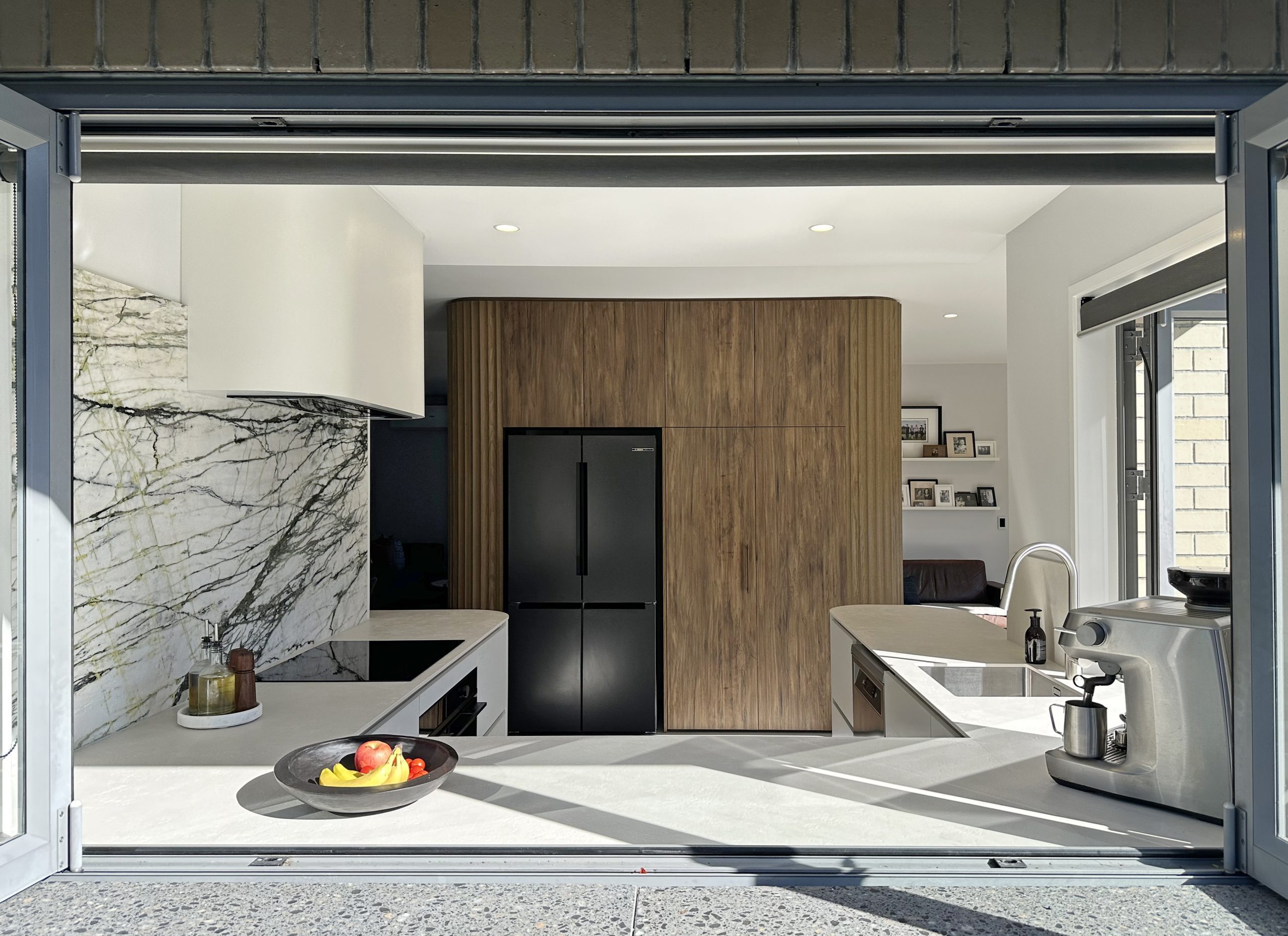 Exterior view of custom Bayswater kitchen by Fluid Interiors, featuring tall Ripple Flex oak panels, curved Aged Walnut cabinetry, built-in fridge and pantry, and sculpted rangehood.