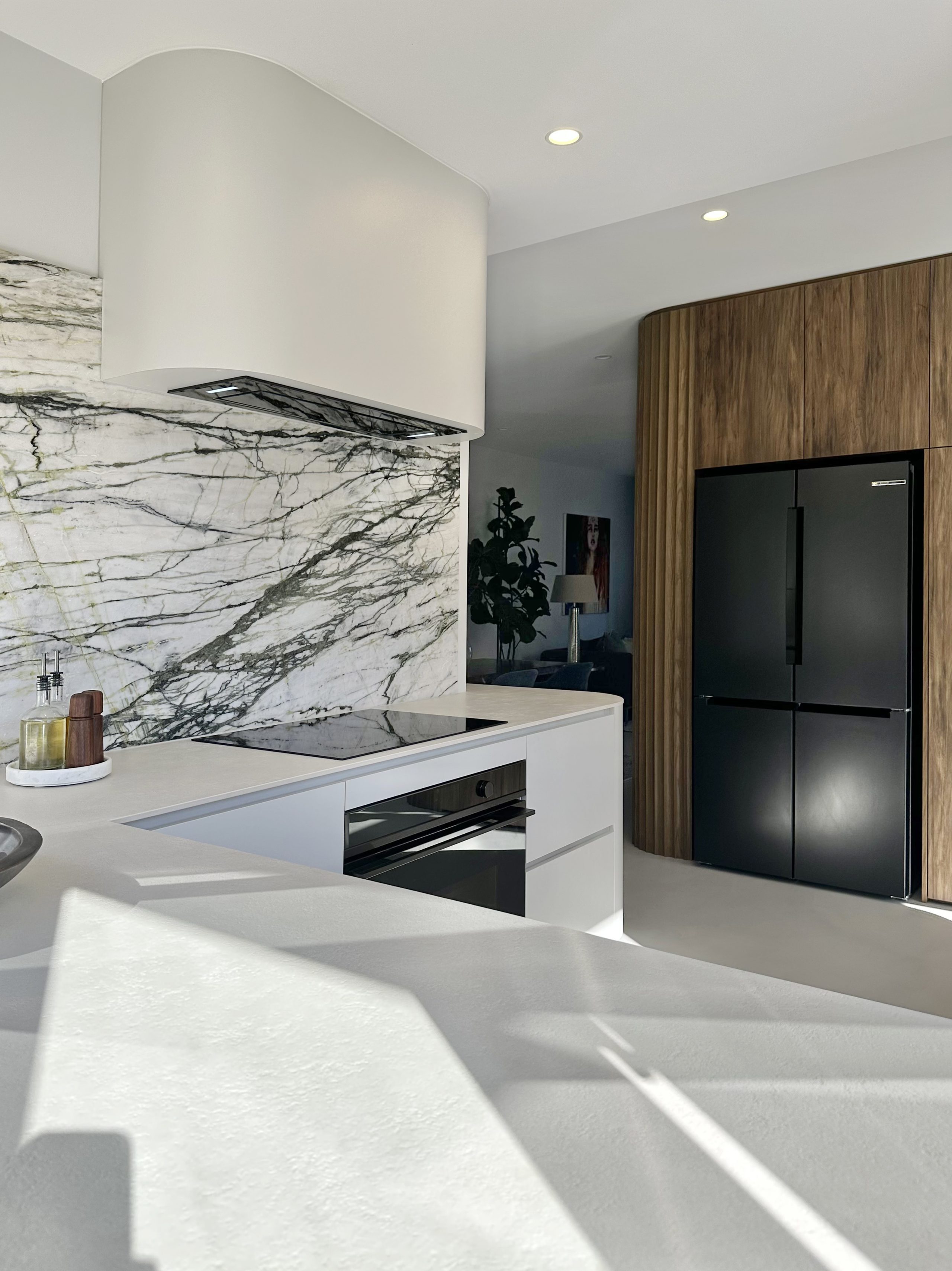 Melteca Baikal Natural base cabinetry with curved Calacatta Verde marble splashback, custom curved rangehood, and tall Ripple Flex oak panels in the Bayswater kitchen by Fluid Interiors.