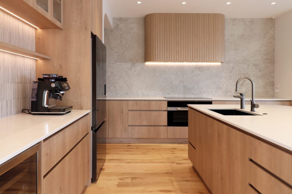 View of custom fluted oak rangehood with integrated extractor fan, framed by large-format tile splashback and LED-lit shelving in a modern Auckland kitchen
