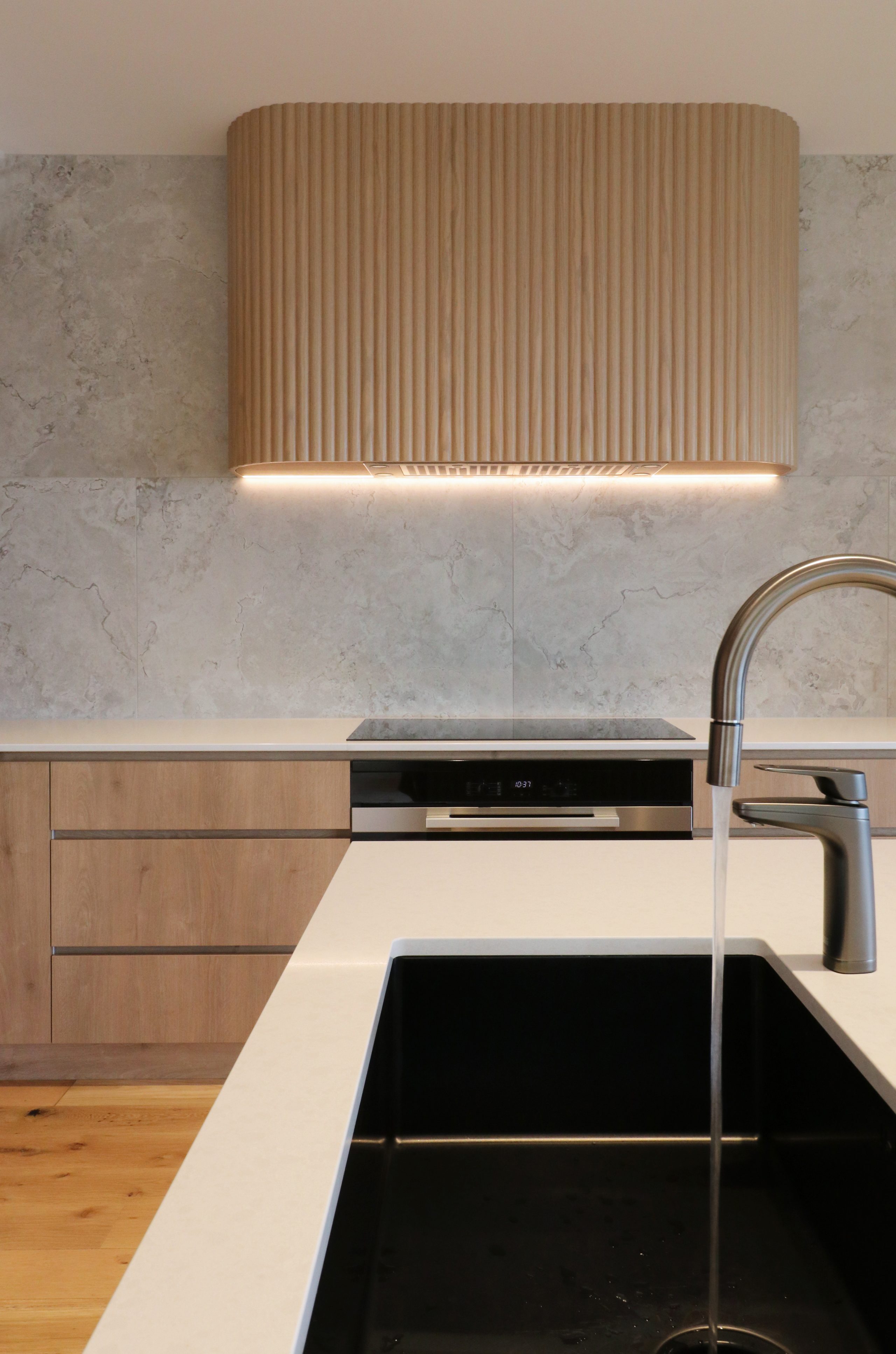 View looking toward custom fluted oak rangehood with integrated extractor, featuring a kitchen tap running water over the sink in a bespoke Auckland kitchen.
