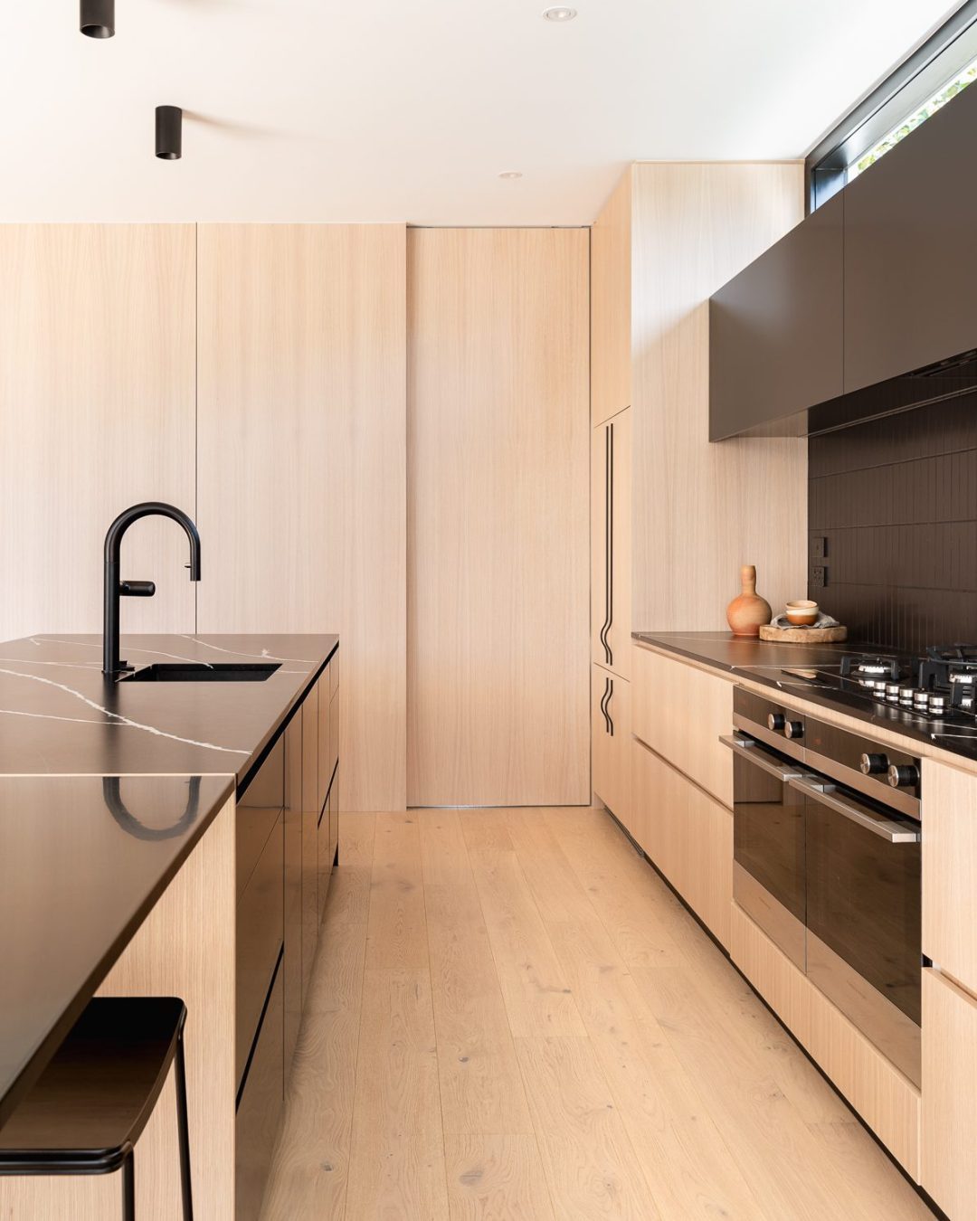 View from Mt Eden kitchen toward scullery, featuring American oak veneer-clad wall and sliding door, detailed and installed by Fluid Interiors.