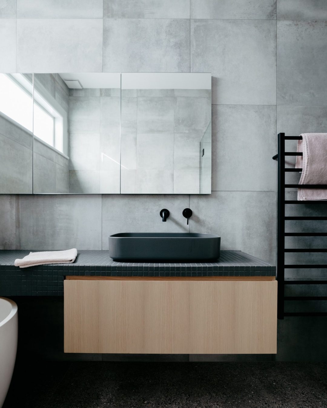 Straight-on view of custom handleless oak vanity with black tiled benchtop, black basin, and taps in Herne Bay bathroom by Fluid Interiors.