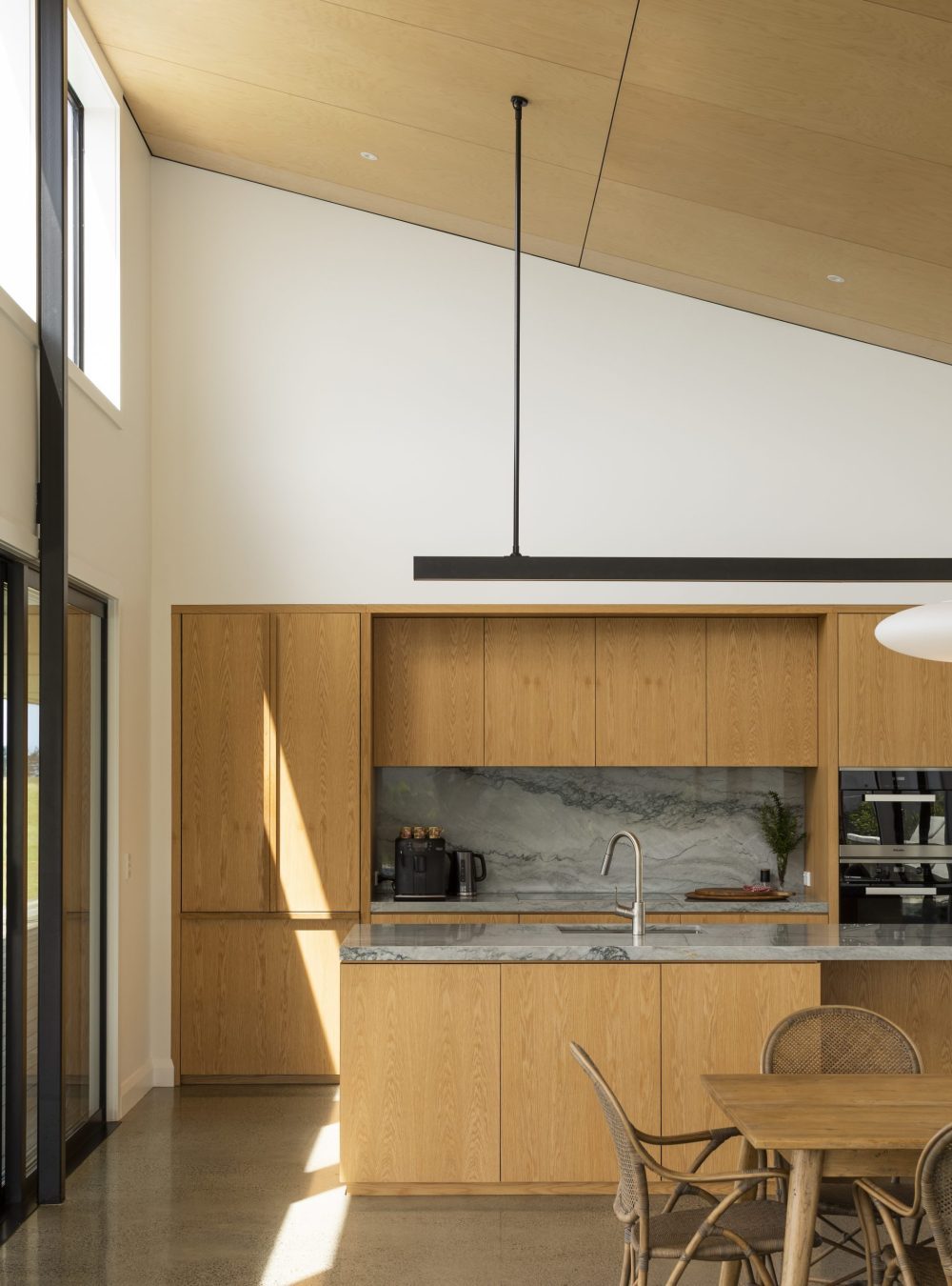 Kitchen view from the back of the island featuring Marlin Grey quartzite benchtops and splashback with custom American oak cabinetry and integrated fridge with custom handles