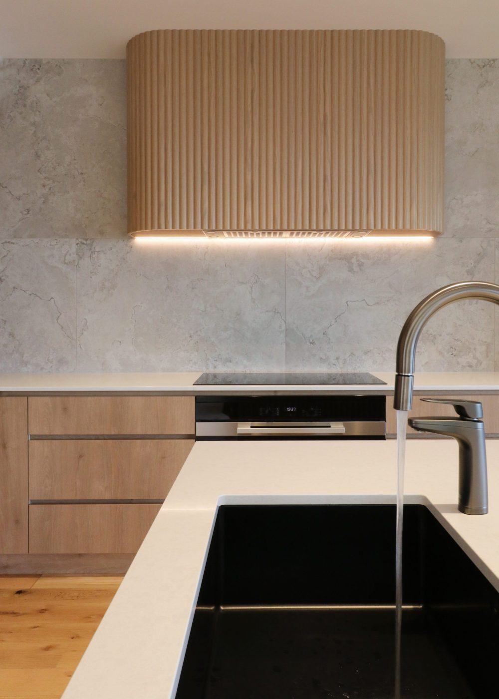 View looking toward custom fluted oak rangehood with integrated extractor, featuring a kitchen tap running water over the sink in a bespoke Auckland kitchen.