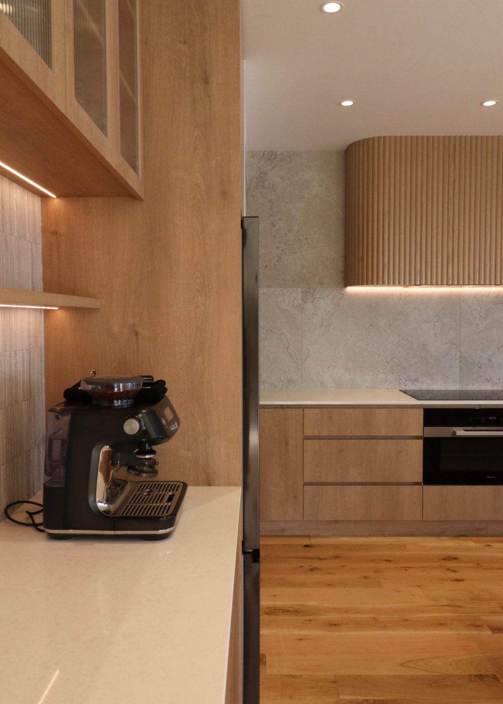 View from the coffee machine area looking toward the custom fluted oak rangehood and integrated extractor in a modern Auckland kitchen.