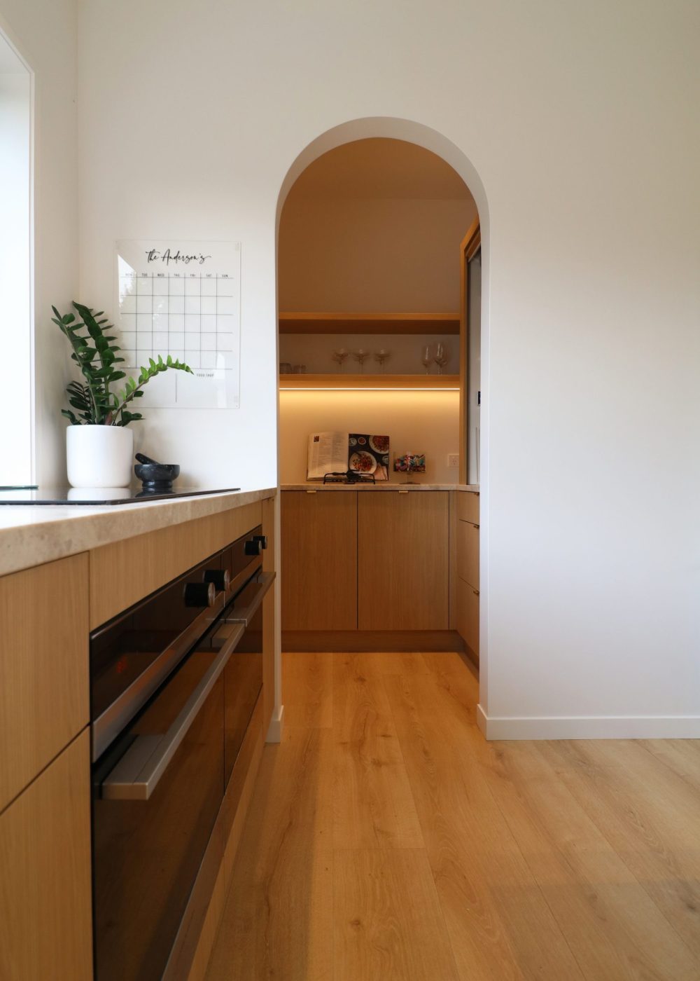 Close-up of curved scullery entry in custom Wainui kitchen by Fluid Interiors, featuring LED-lit open shelves and warm-toned cabinetry.