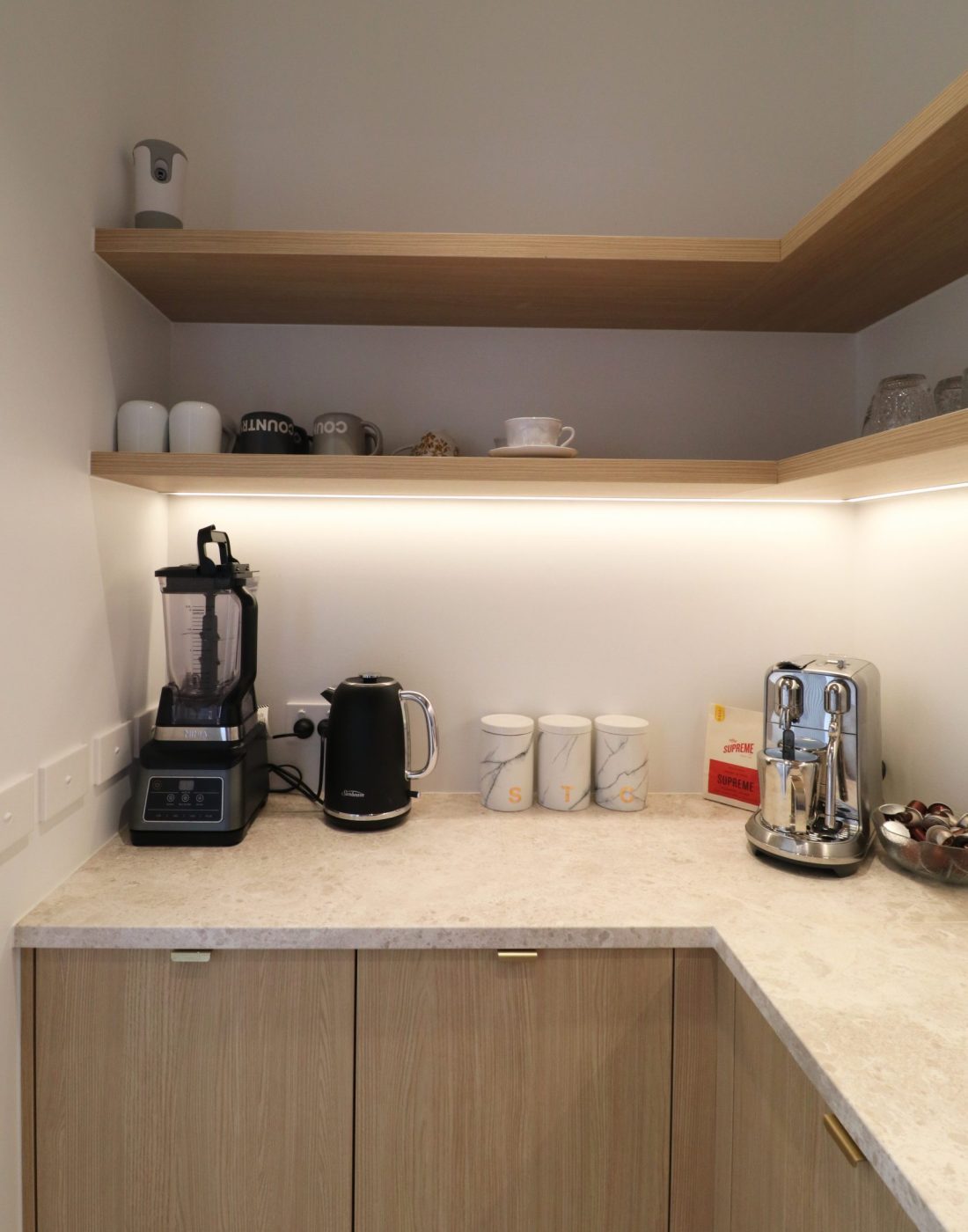 Straight-on view of scullery in Wainui kitchen by Fluid Interiors, featuring coffee station with appliance storage, jug, and open shelving in aged ash Melteca Puregrain cabinetry.